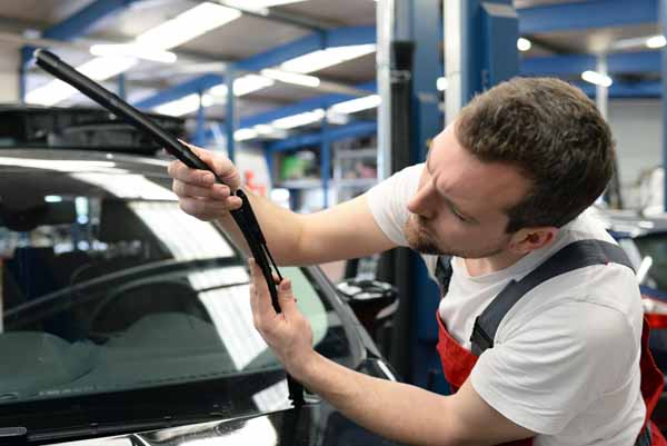 A mechanic in a red apron installs a wiper blade on a car