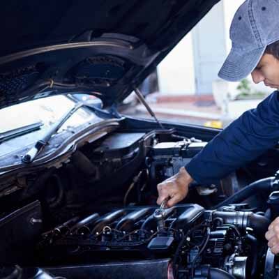 A mechanic in a cap and blue uniform is working on a car engine