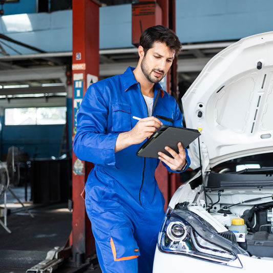 A mechanic in blue coveralls writes on a tablet